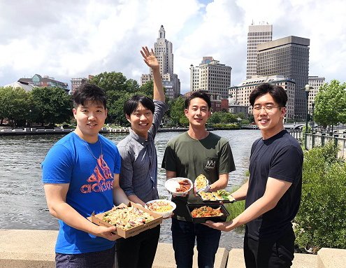 four men holding take out food in front of city scape