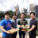 four men holding take out food in front of city scape