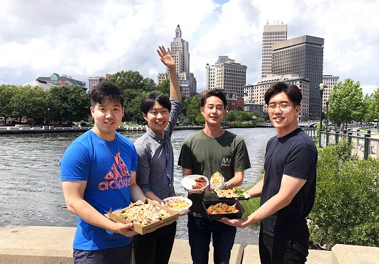 four men holding take out food in front of city scape