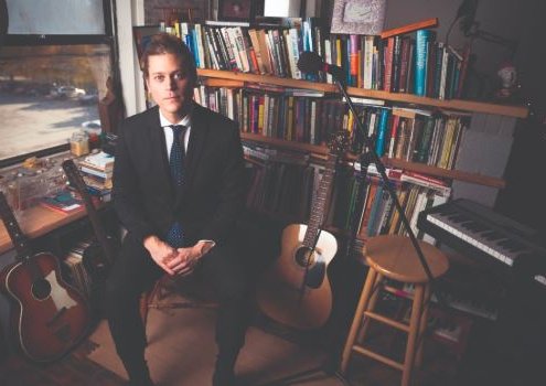 bill bartholomew promo shot sitting surrounded by guitars