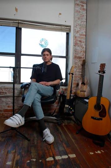 bill bartholomew sitting behind a mic with guitars to his side