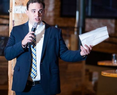man speaking into microphone and holding paper